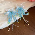 Close-up of blue and yellow beaded floral tassel earrings on a wooden background - Blue Yellow White