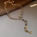 Dettaglio ravvicinato di una collana dorata a due strati con delicati ciondoli a rosa - Oro