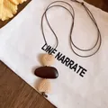Close-up of an ethnic style necklace with heart-shaped and pebble pendants on a bag - Woven Heart Irregular Style (HN12225) / Brown