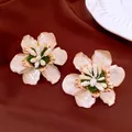 Nahaufnahme eleganter Ohrstecker in Blumenform aus weißer Emaille mit Goldakzenten. - Weiß