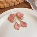 Detailed close-up view of pink enamel flower earrings with gold-toned petal drops on a plate. - Pink