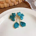 Detailed view of teal floral enamel earrings with golden tassels on a white plate - Blue