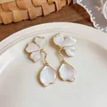 Macro detail showing the intricate white enamel flower petal drop earrings on a ceramic plate - White