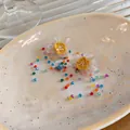 Close-up of handmade floral earrings with colorful beaded tassels on a ceramic plate. - Colorful