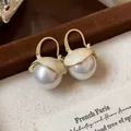 Detailed view of elegant French style enamel gold earrings with white pearls on a tray - Hoop Buckle Style / Gold with White Pearl