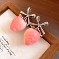 Close-up of sweet pink strawberry earrings with sparkling zircon-encrusted bows. - Pink