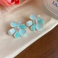 Macro detail showing elegant light blue textured flower earrings with clear zircon center - Blue
