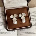 Primer plano detallado de elegantes pendientes de flores y perlas en un joyero de terciopelo - Plata & Blanco (Silver Earring Post)