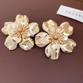 Detailed view of oversized glossy gold flower stud earrings on leather background. - Gold