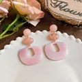 Dettaglio ravvicinato di orecchini geometrici in acetato rosa su un piatto bianco - Stile geometrico retrò / Rosa