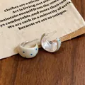 Pendientes de aro en forma de C de esmalte crema con lunares azules sobre madera. - Gris