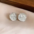 Close-up view of matte silver round stud earrings featuring a vintage embossed horse - Silver