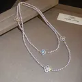 Close-up detail of an elegant pearl necklace featuring sparkling CZ inlaid clover pendants - Necklace / Gold