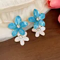Dettaglio di orecchini a fiore smaltati blu e bianchi con strass - Perno in acciaio inossidabile - Oro / Blu