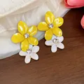 Dettaglio di orecchini a forma di fiore in smalto giallo e bianco con strass lucidi - Perno in acciaio inossidabile - Oro / Giallo