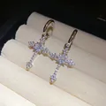 Detailed close-up view of silver zircon cross pendant earrings on a beige jewelry display - Cross Pendant Style (HE32344) / Silver