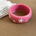 Gros plan d'un bracelet jonc en résine rose orné de jolis motifs d'étoiles blanches. - Rose