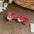Nahaufnahme von Retro-Ohrsteckern mit rosa Emaille-Orchideen auf Holzoberfläche - Rosa