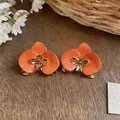Detailaufnahme von orangefarbenen Emaille-Blumenohrringen mit eleganten goldfarbenen Akzenten - Orange