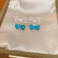 Close-up of bow earrings with blue heart crystals and pearl accents in a jewelry box - Earrings Only (HE34141) / Silver-Blue