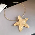 Close-up detail of a large gold-toned starfish pendant on a thin metal choker necklace. - Starfish Pendant Choker / Gold