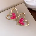 Primer plano de pendientes de corazón dorados con esmalte rosa sobre fondo beige - Rosa
