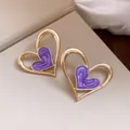 Primer plano de elegantes pendientes de corazón dorados con esmalte de mármol púrpura - Púrpura