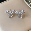 Close-up detail of 18k gold plated bow-knot pearl earrings with heart-shaped crystal - Silver
