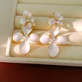 Detailed view of elegant white enamel flower earrings with sparkling rhinestone centers - White