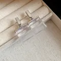 Close-up of silver-toned studs with transparent square resin pendants on cream jewelry box. - Earrings / Silver-White