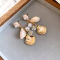 Vista detallada de pendientes dorados con perlas y conchas sobre terciopelo gris - Estilo Colgante Poste de Plata / Marrón dorado