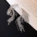 Primer plano de pendientes de borla de plata geométrica con cadenas de cuentas en un libro - Estilo de borlas retorcidas geométricas / Plateado