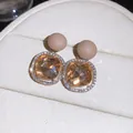 Close-up detail view of champagne gemstone earrings with diamond halo and matte studs - Brown