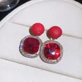 Detail view of luxury red gemstone stud earrings with sparkling rhinestone halo. - Red