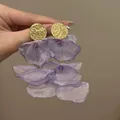 Dettaglio di orecchini a fiore in tessuto viola con perni dorati dalla trama lucida. - Stile a Petali in Tessuto Multistrato / Viola