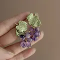 Primo piano di eleganti orecchini a forma di uva con perline viola e foglie verdi - Stile Orecchino a Forma di Uva / Verde Blu