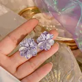 Dettaglio ravvicinato di eleganti orecchini a lobo a fiore viola cangianti - Stile Bottone a Fiore 3D / Viola