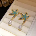 Detailed view of gold starfish earrings with blue rhinestones and dangling white pearls. - Gold-Blue
