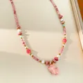 Close-up of a pink ceramic puppy charm on a beaded pearl necklace with golden accents. - Necklace-Pink