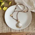 Detail view of Bohemian shell necklace on white plate with summer beach holiday vibes - Scallop / Brown