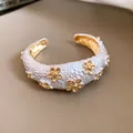 Close-up of elegant white textured open cuff bracelet with gold flower ornaments and metallic finish - Floral Relief Style / Gold/White