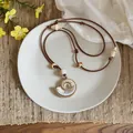Close-up of a Bohemian spiral shell pendant necklace displayed on a white plate. - Shell / Brown