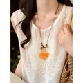 Close-up detail of bohemian orange flower pendant necklace worn over white lace top - Coffee-Orange