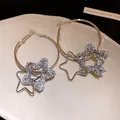 Macro view of elegant silver hoop earrings featuring double star-shaped pendants - Silver (Silver Earring Post)