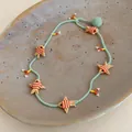 Close-up detail of handmade glass beaded necklace with orange fish charms on a plate - Colorful