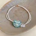 Close-up of a handcrafted white pearl necklace with a turquoise beaded floral detail. - White-Blue