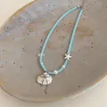 Macro detail of blue glass bead necklace featuring a delicate shell and starfish pendant - Blue-White