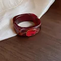 Detail van een donkerrode gemarmerde hars armband met een rode edelsteen in goudkleur. - Vierkante Strass Armring / Rood