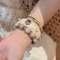 Detailed view of cream resin shell bangle, gold metal ring, and beaded bracelet on wrist - Ivory White (HB6147HB6135)