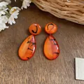 Close-up of French retro orange resin teardrop earrings with black marbled patterns - Brown